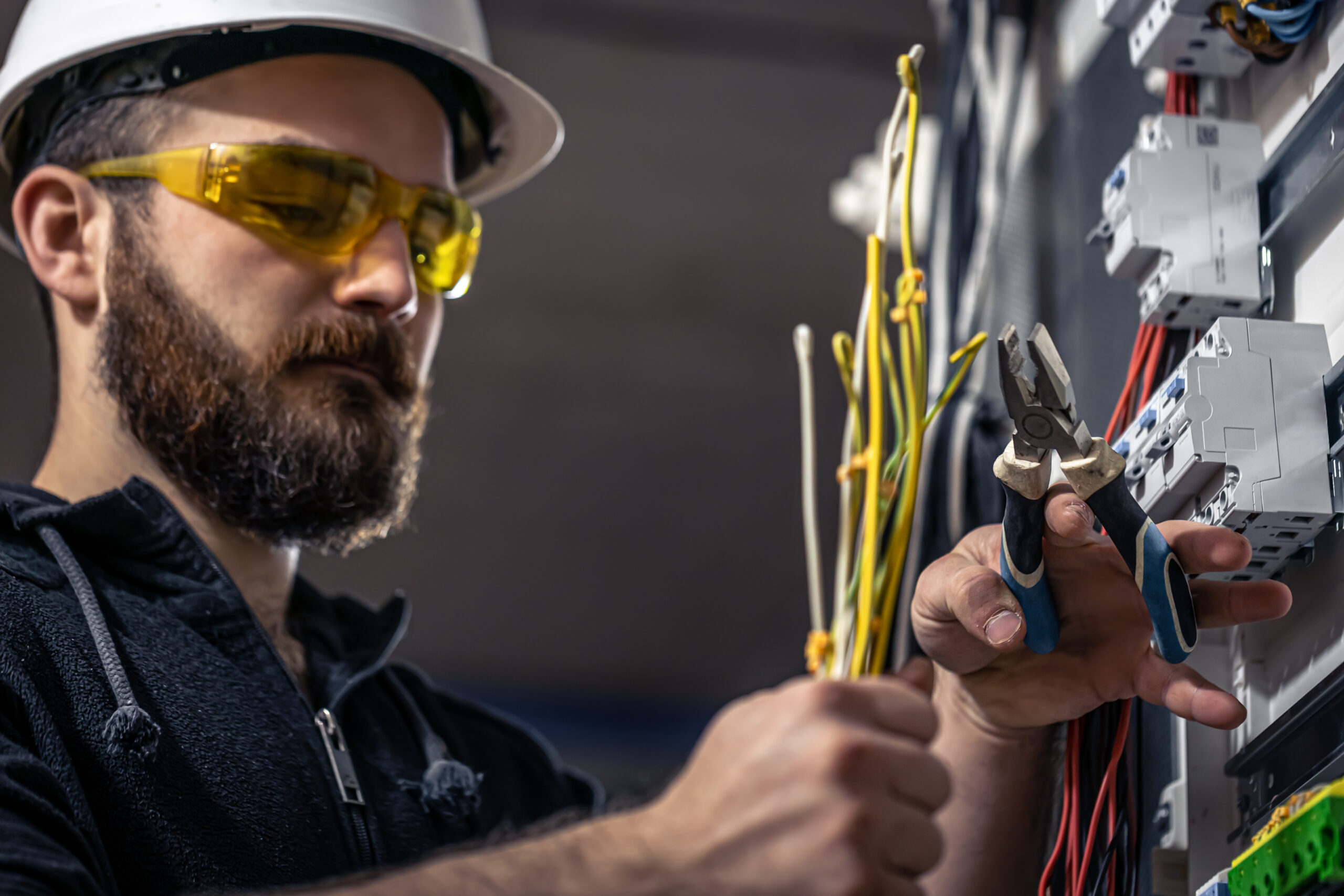 a male electrician works in a switchboard with an electrical connecting cable.